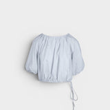 JONES + CO light blue cropped Lotus top with short sleeves, gathered cuffs, and drawstring waist, featuring French knot embroidery.