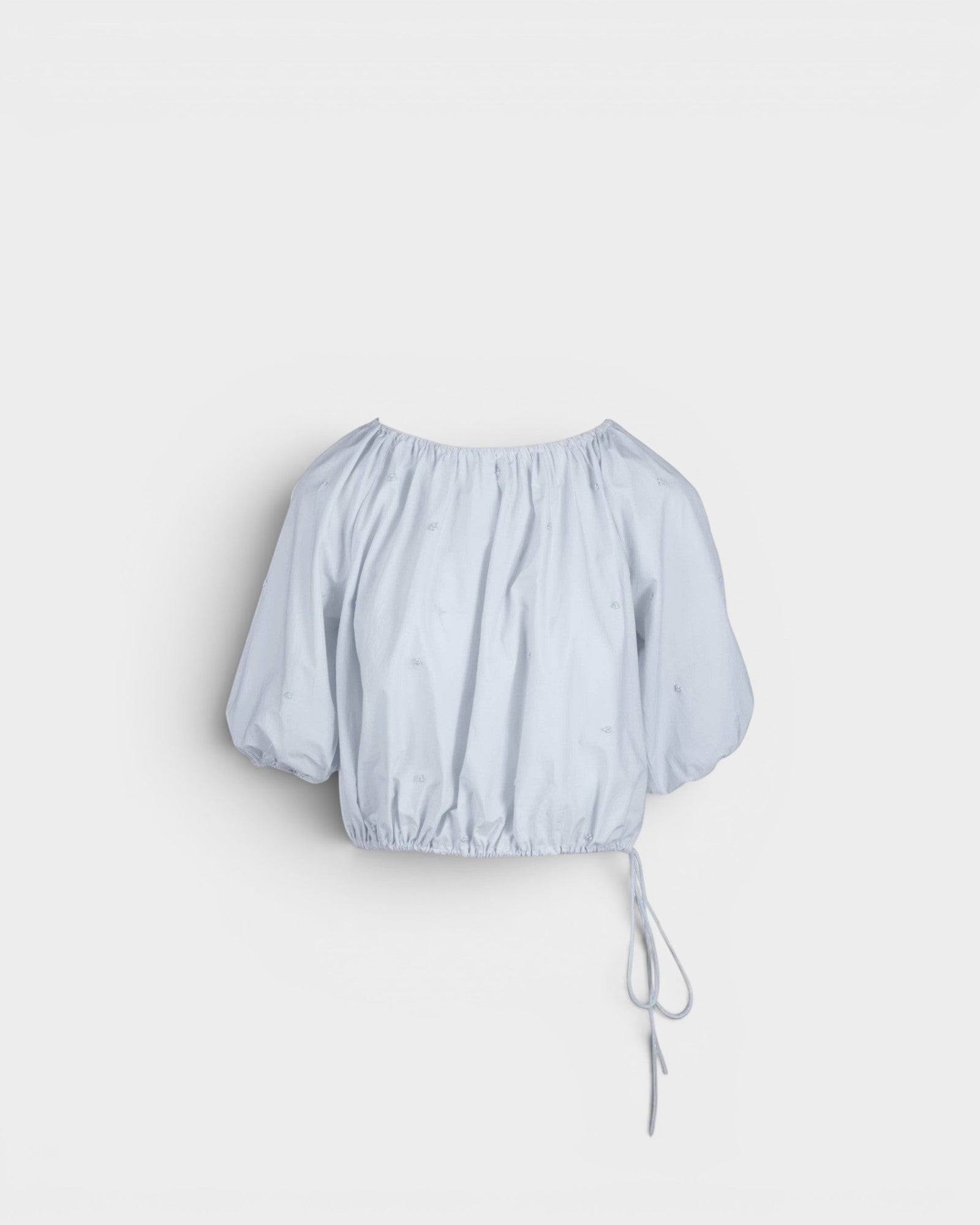 JONES + CO light blue cropped Lotus top with short sleeves, gathered cuffs, and drawstring waist, featuring French knot embroidery.