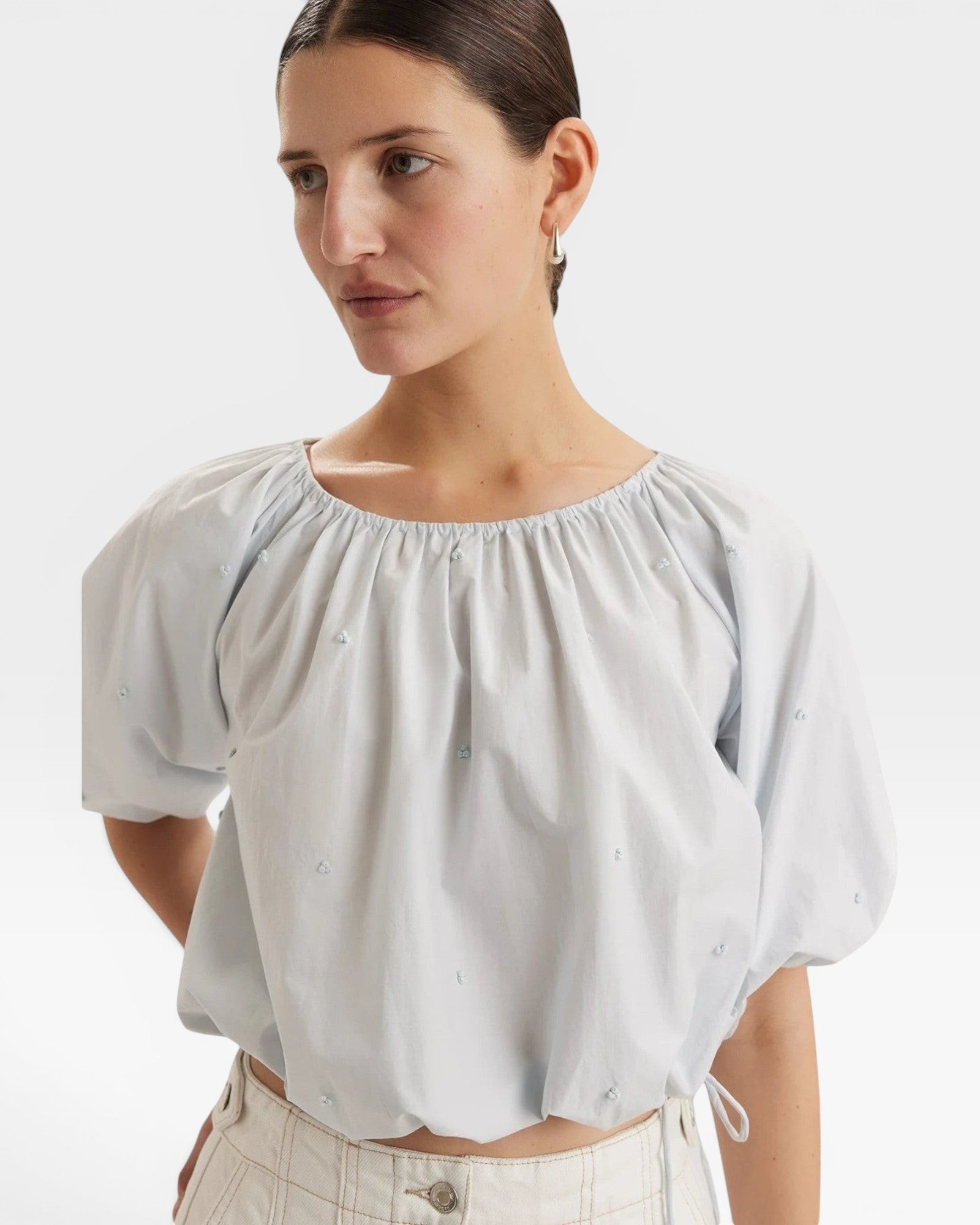 JONES + CO light blue cropped Lotus top with short sleeves, gathered cuffs, and French knot embroidery. Drawstring waist.