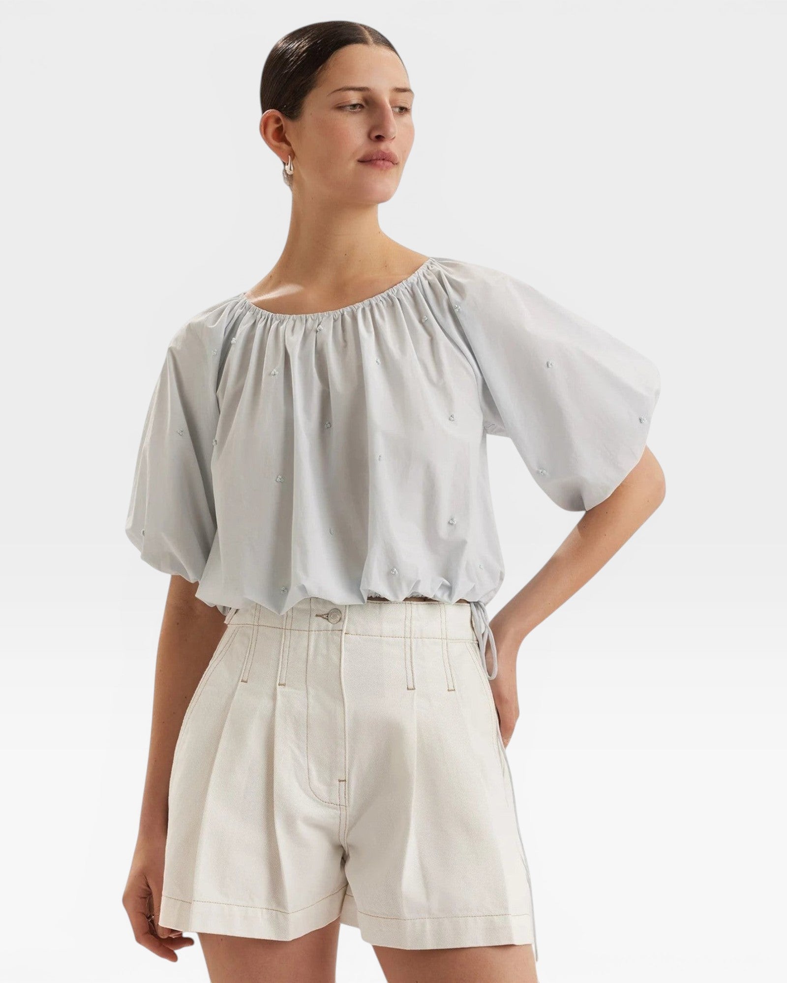 JONES + CO light blue cropped Lotus top with short sleeves, gathered cuffs, and French knot embroidery. Drawstring waist.