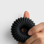 JONES + CO lülala black charcoal and sesame soap bar with a circular, fluted geometric design held in a hand.