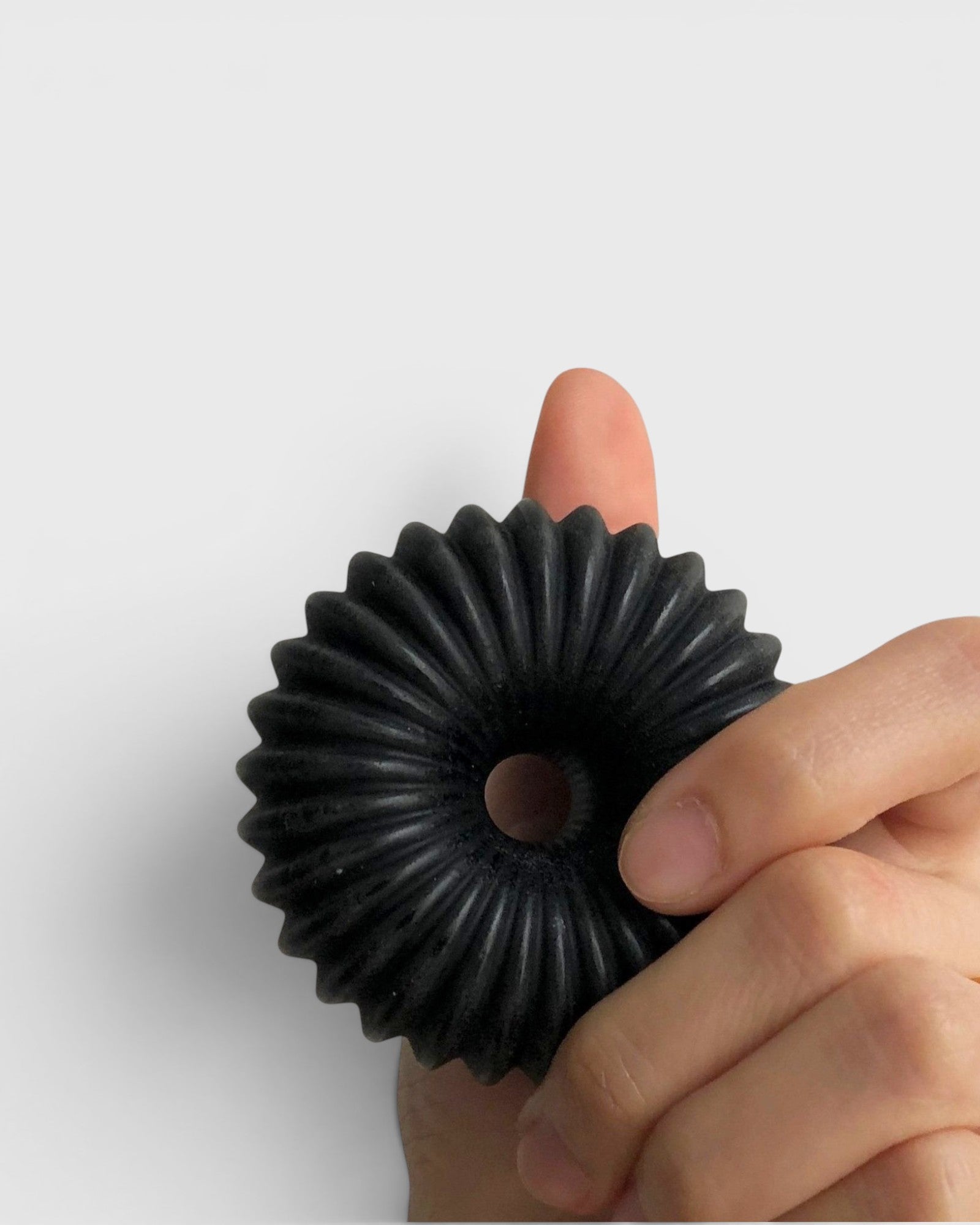 JONES + CO lülala black charcoal and sesame soap bar with a circular, fluted geometric design held in a hand.