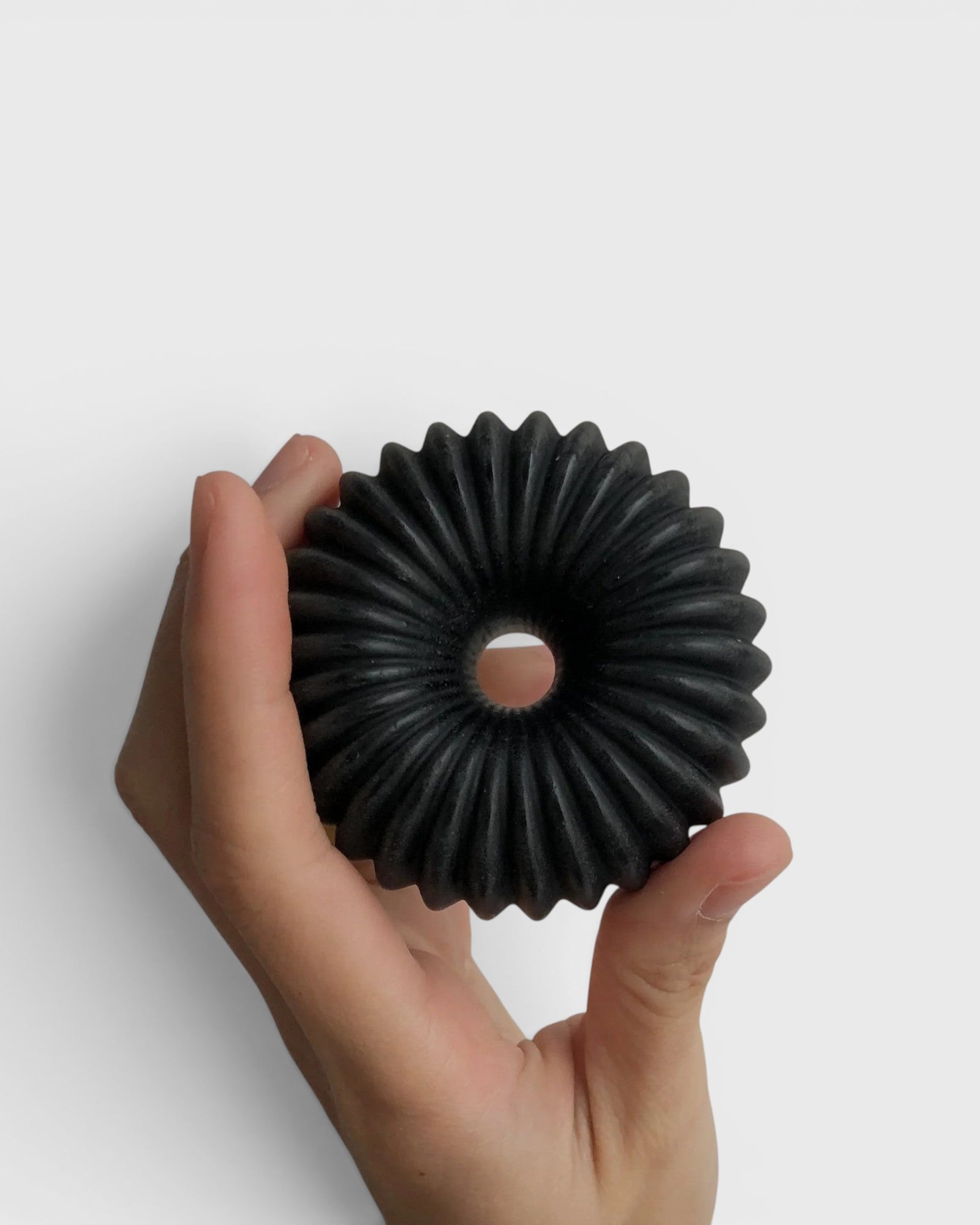 JONES + CO lülala black charcoal and sesame soap bar with a unique circular ribbed design held in a hand.
