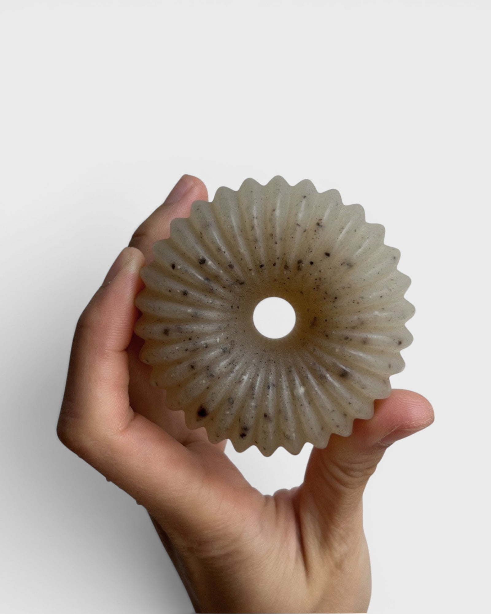 JONES + CO lülala marjoram and sesame soap bar with a translucent, fluted, donut-like shape held in a hand.
