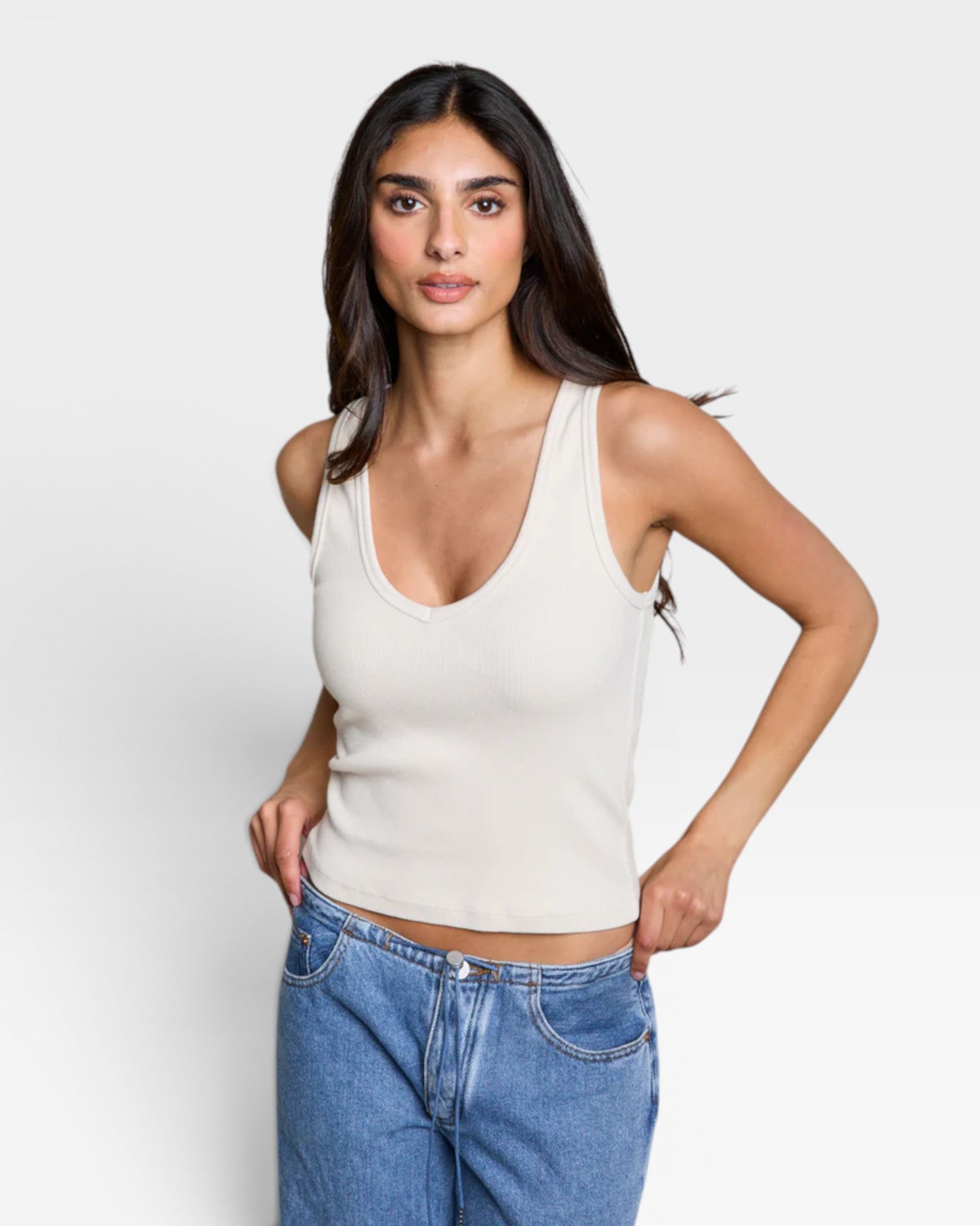 JONES + CO Maria V Neck tank top in sugar white ribbed fabric with a v-neckline. Model wears blue jeans.