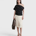 Model wearing a black JONES + CO Mata one-shoulder organic cotton blouse with an asymmetric neckline.