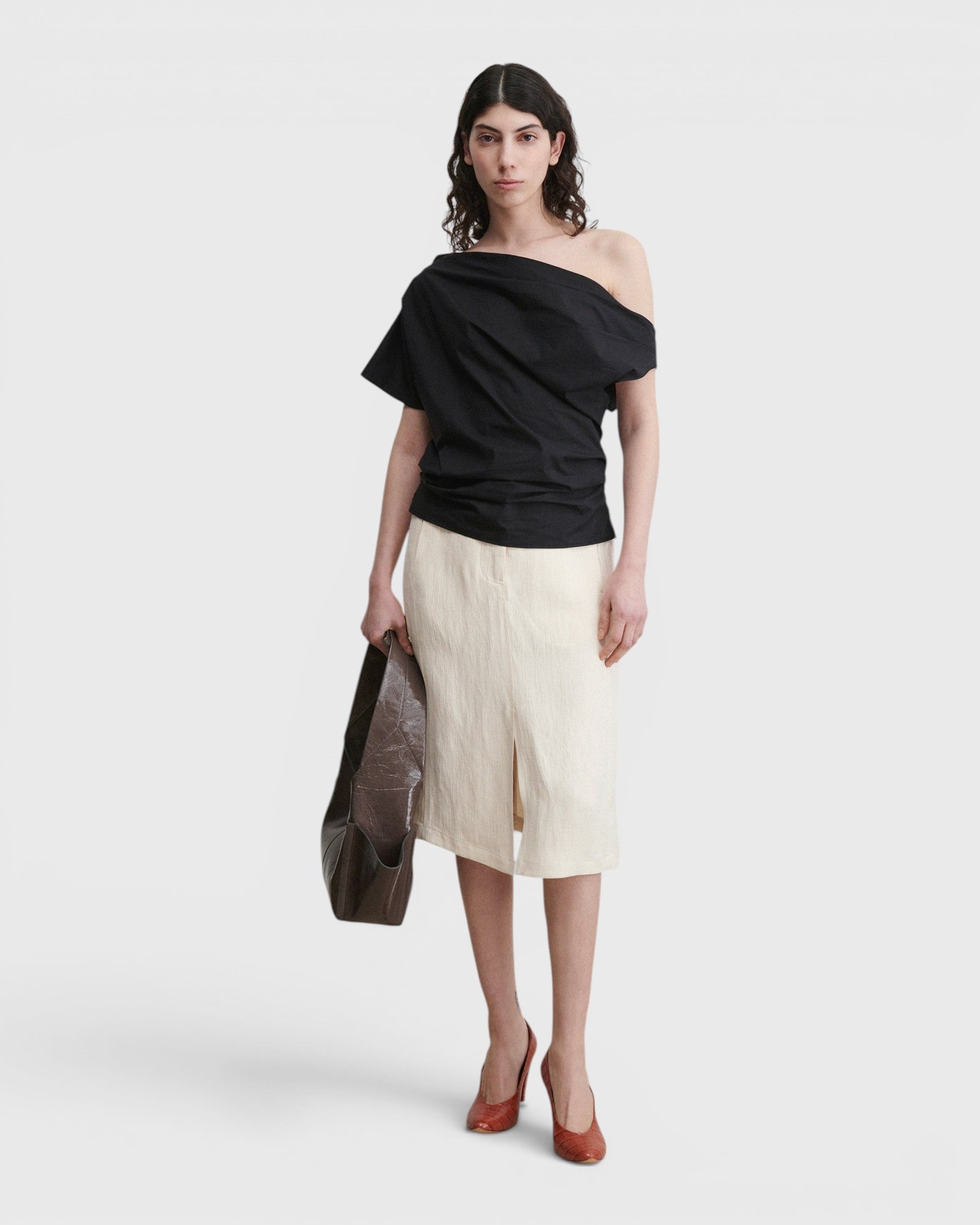Model wearing a black JONES + CO Mata one-shoulder organic cotton blouse with an asymmetric neckline.