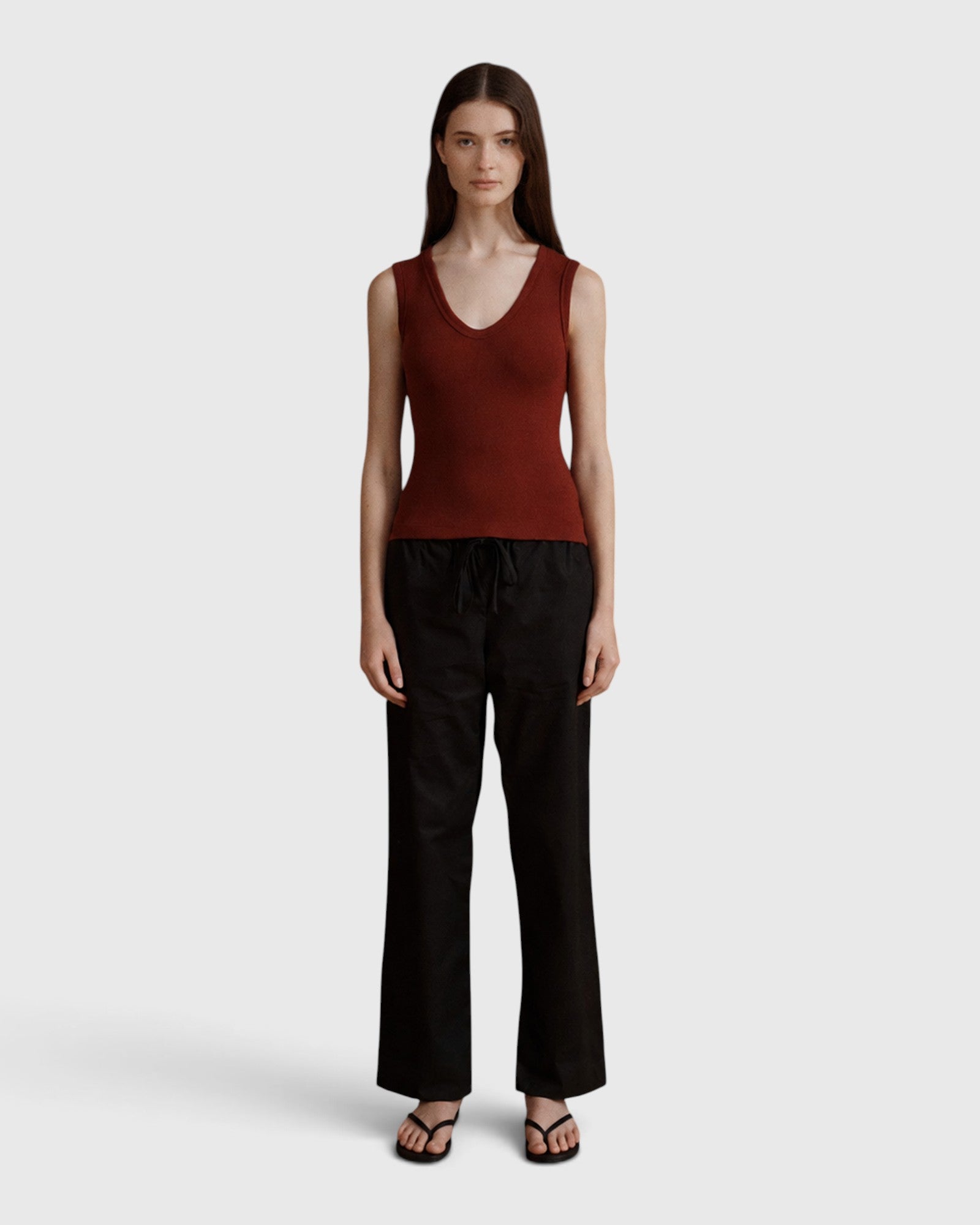 Model wearing JONES + CO merlot ribbed knit Kana Tank with deep scoop neckline and fluid fit against grey background
