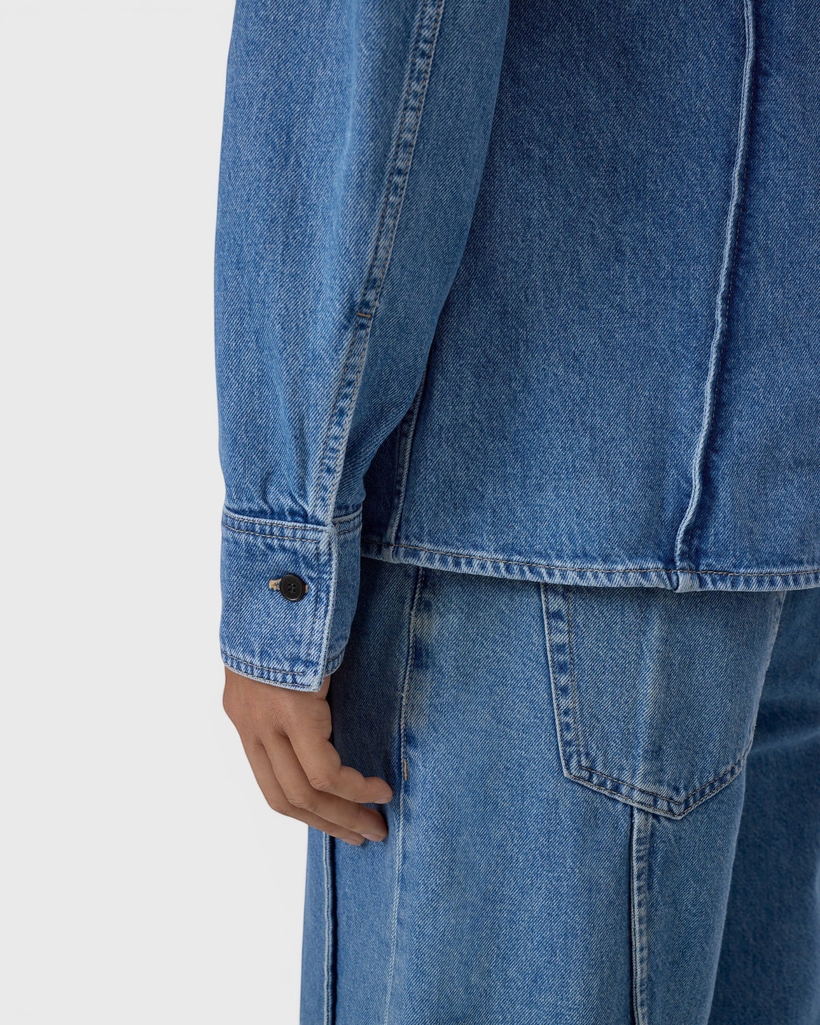 JONES + CO mid blue denim shirt featuring curved seam detailing and buttoned cuffs in a fitted silhouette.