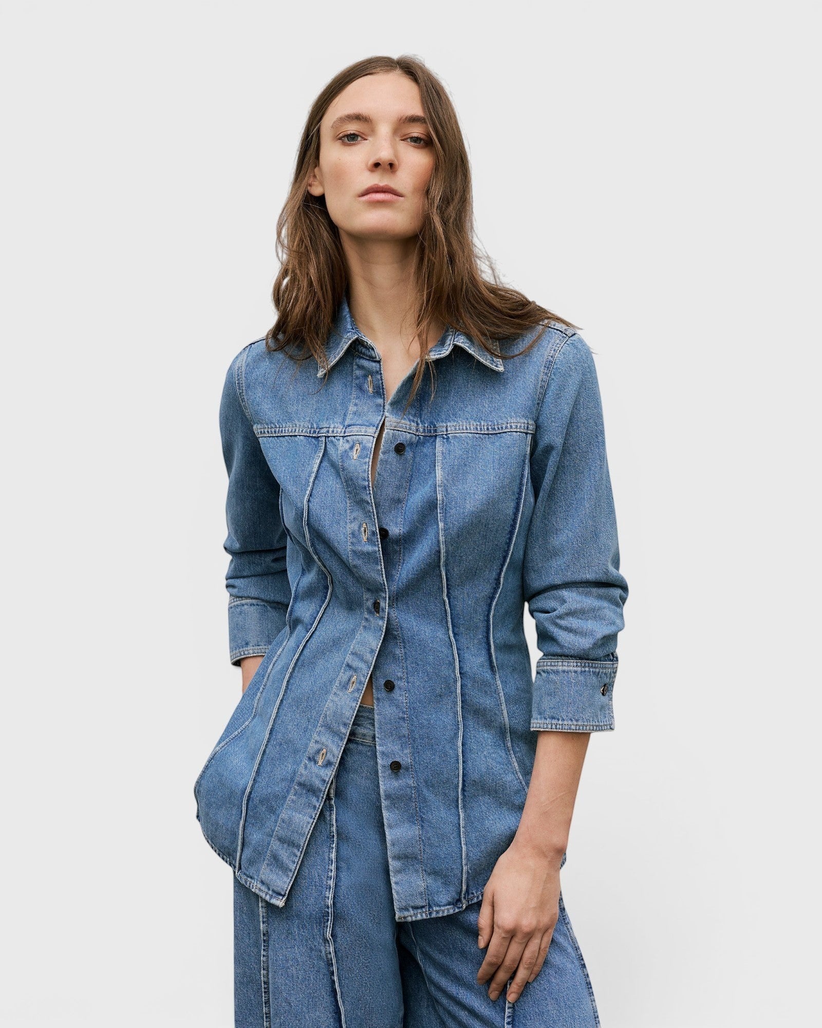 JONES + CO mid blue denim shirt with curved seams, pointed collar, and button-front closure on a female model.