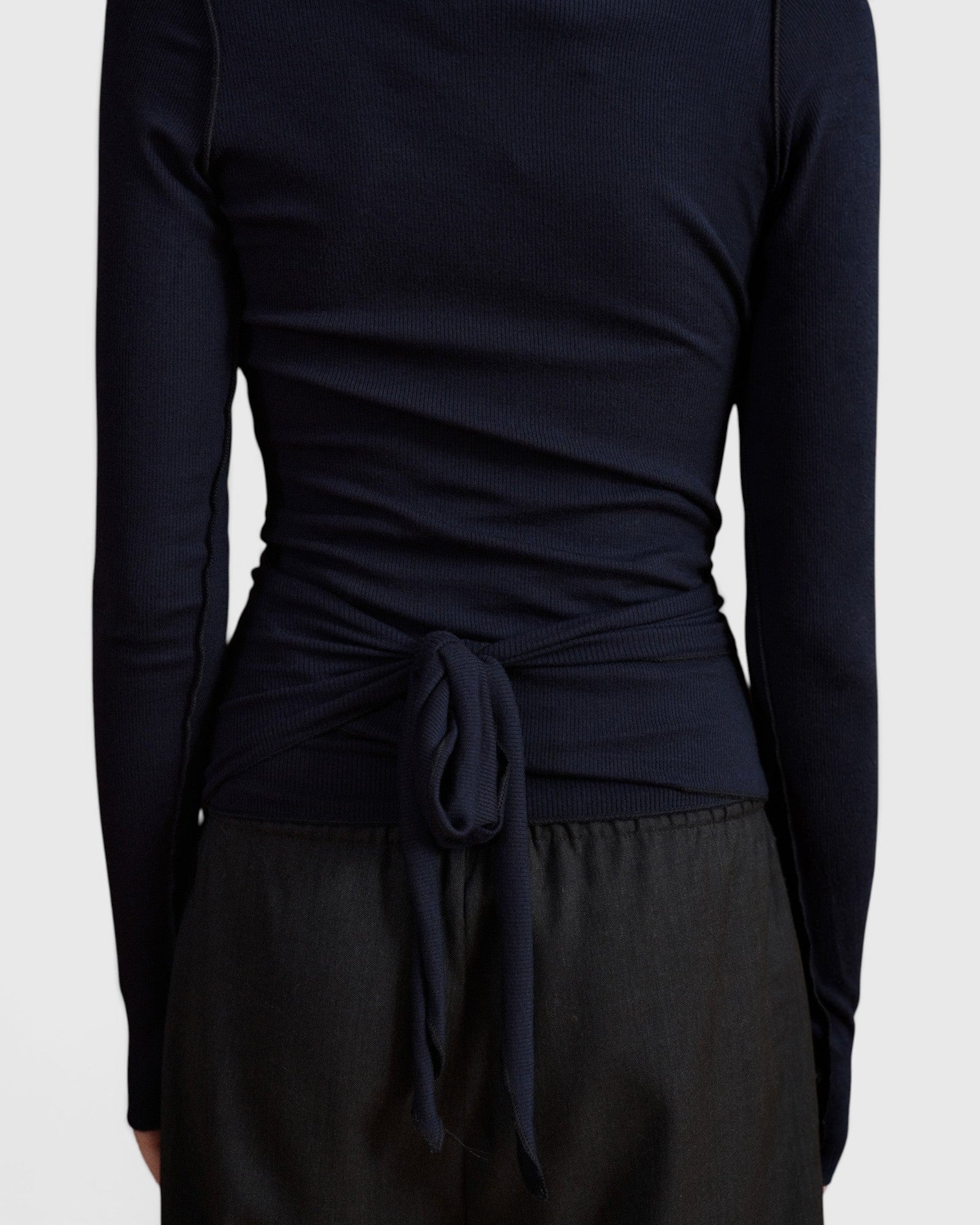 Back view of JONES + CO Margot wrap top in midnight blue knit fabric with a tied waist detail.