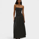 Model wearing JONES + CO black and off-white polka dot Mira maxi dress with a smocked bodice and spaghetti straps.
