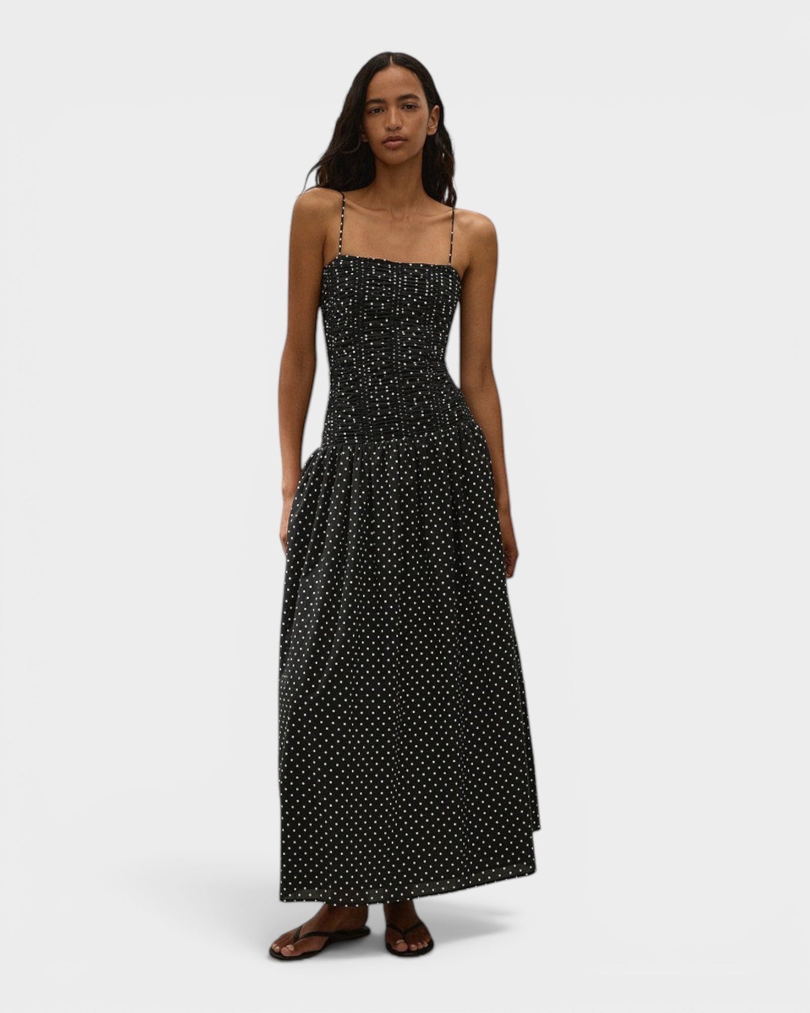 Model wearing JONES + CO black and off-white polka dot Mira maxi dress with a smocked bodice and spaghetti straps.