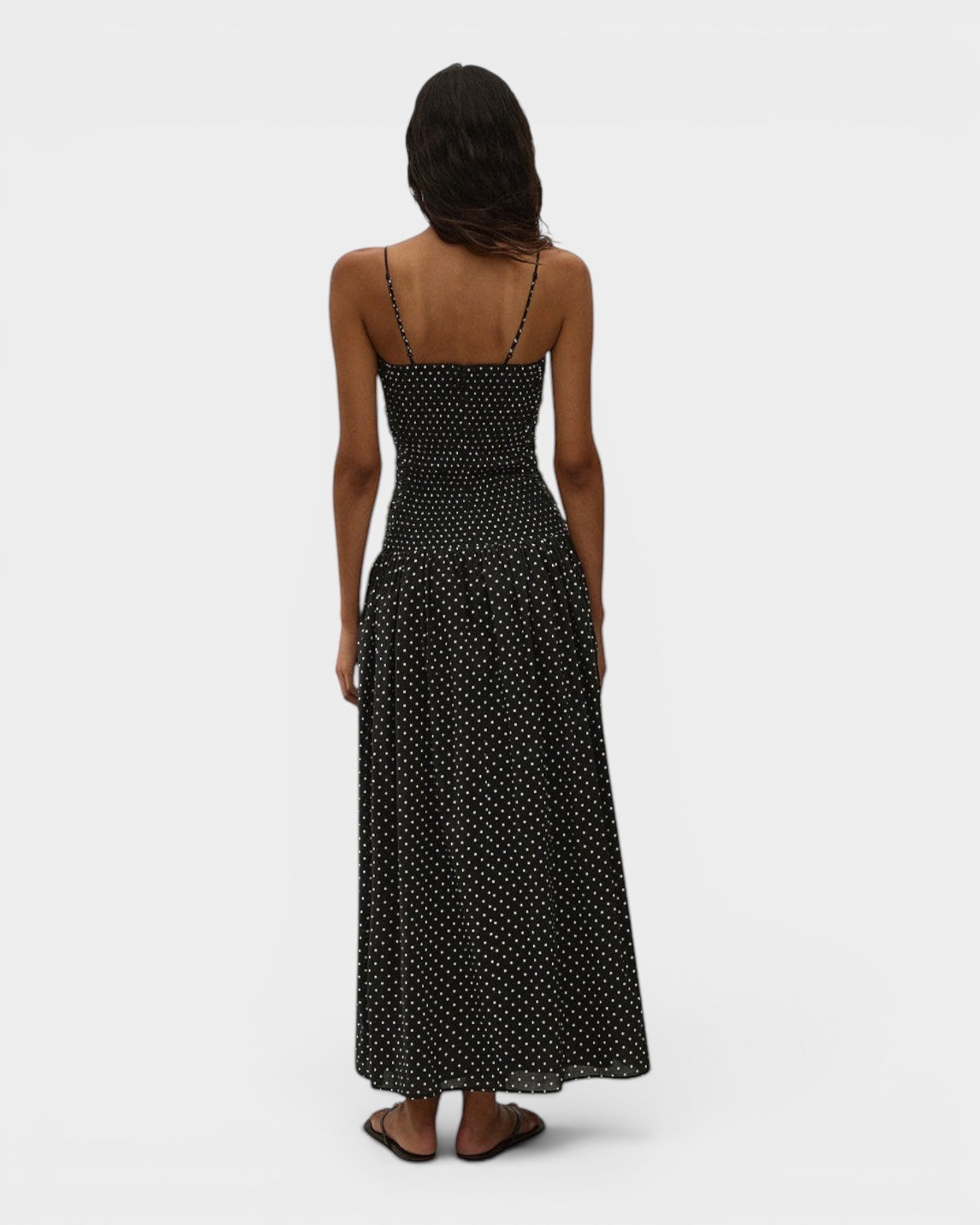 Back view of JONES + CO Mira maxi dress in black with off-white polka dots, featuring spaghetti straps and smocking.