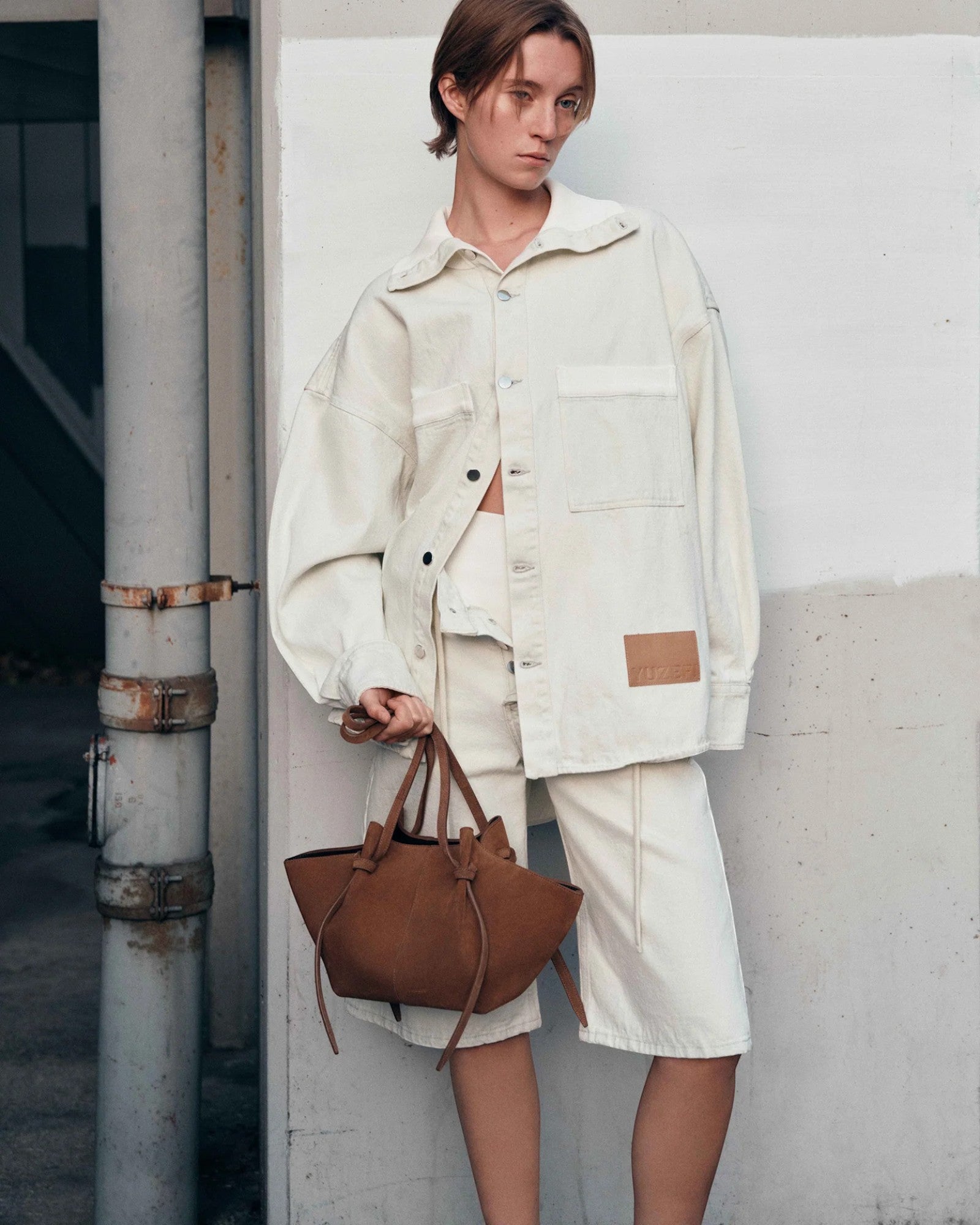 JONES + CO Mochi tote bag in cognac Italian suede with organic curves and knot details held by a model in cream denim