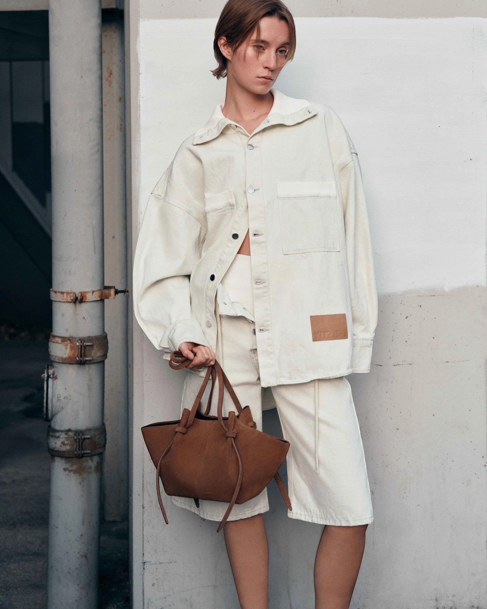 JONES + CO Mochi tote bag in cognac Italian suede with organic curves and knot details held by a model in cream denim