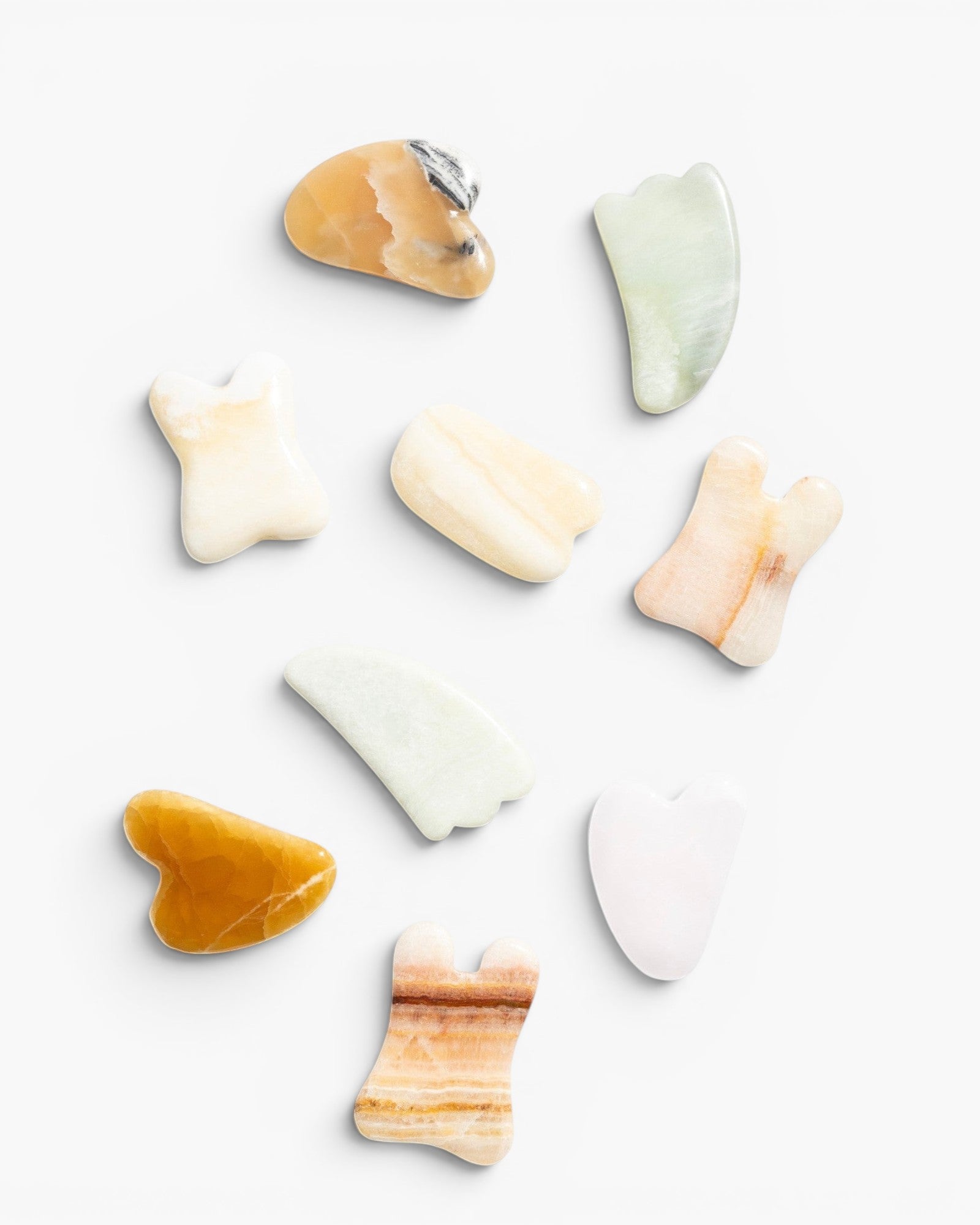 JONES + CO Natural Gua Sha Stones in various shapes and earthy tones like jade green, peach, and amber for depuffing and improving circulation.