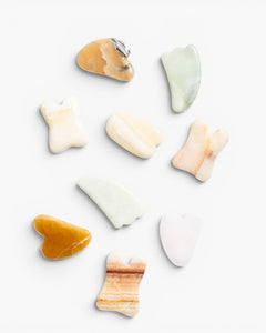 JONES + CO Natural Gua Sha Stones in various shapes and earthy tones like jade green, peach, and amber for depuffing and improving circulation.