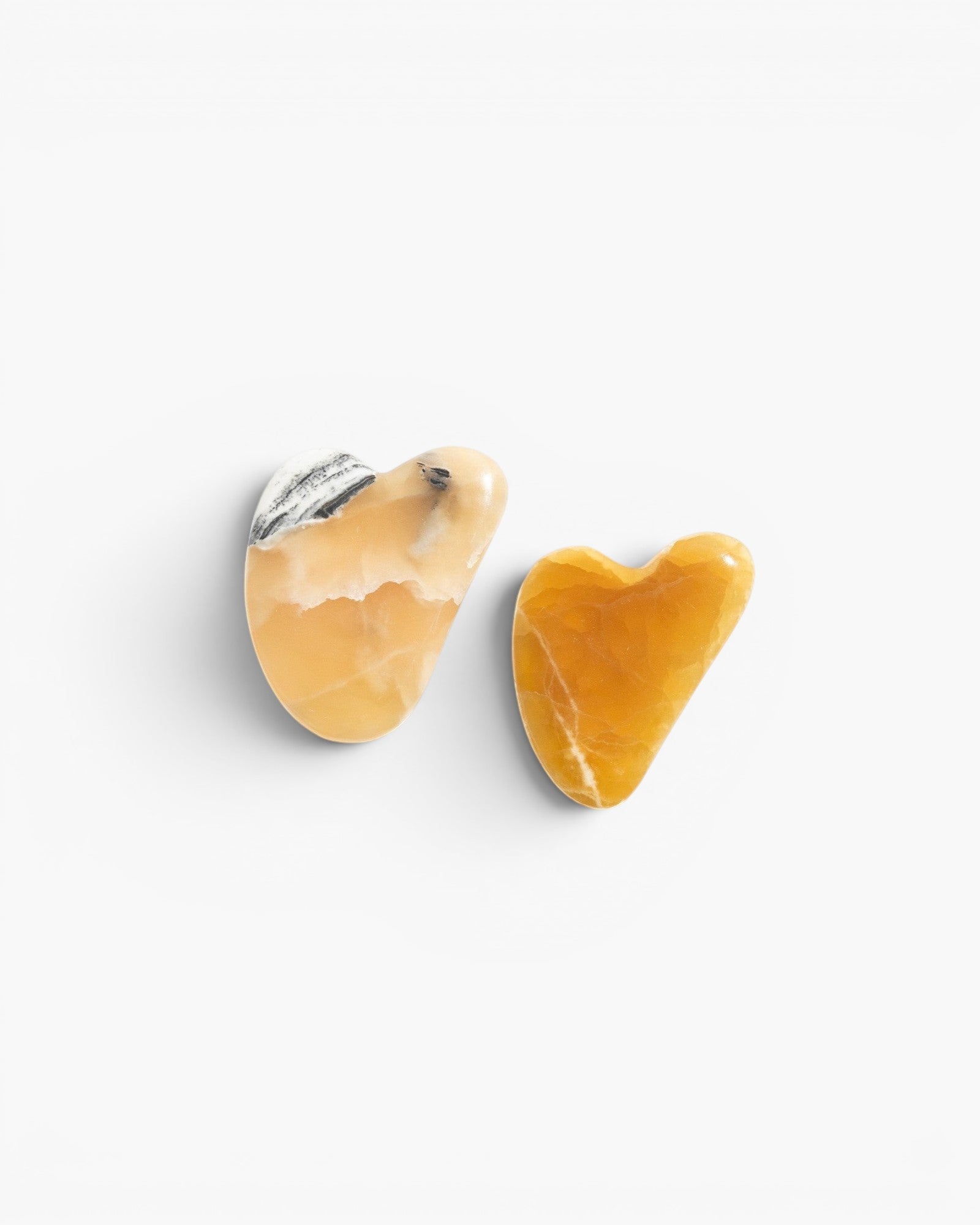 JONES + CO natural gua sha stones in warm yellow and white with black veining, heart-shaped for facial massage.