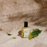 JONES + CO No.02 Le Long Fond perfume oil in a clear glass bottle with a black cap, surrounded by greenery.