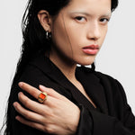 JONES + CO Nocturne Time Ring in 18K deep gold-plated stainless steel with a flame-colored crystal on a model's hand.