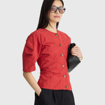 JONES + CO Noor red crew-neck top with button front and short puff sleeves worn by a model with black sunglasses.