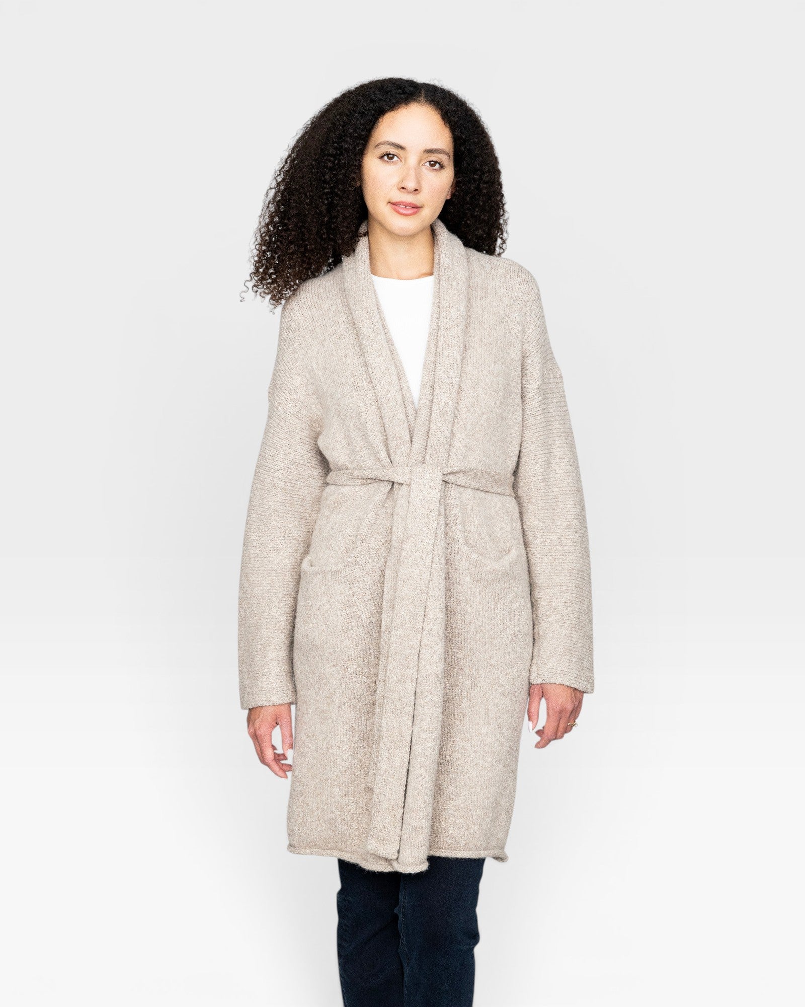 JONES + CO oatmeal alpaca wool blend sweater coat with belt and pockets, worn by a woman with curly hair.