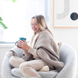 JONES + CO oatmeal alpaca wool blend throw blanket draped over a woman sitting in a chair with a mug.