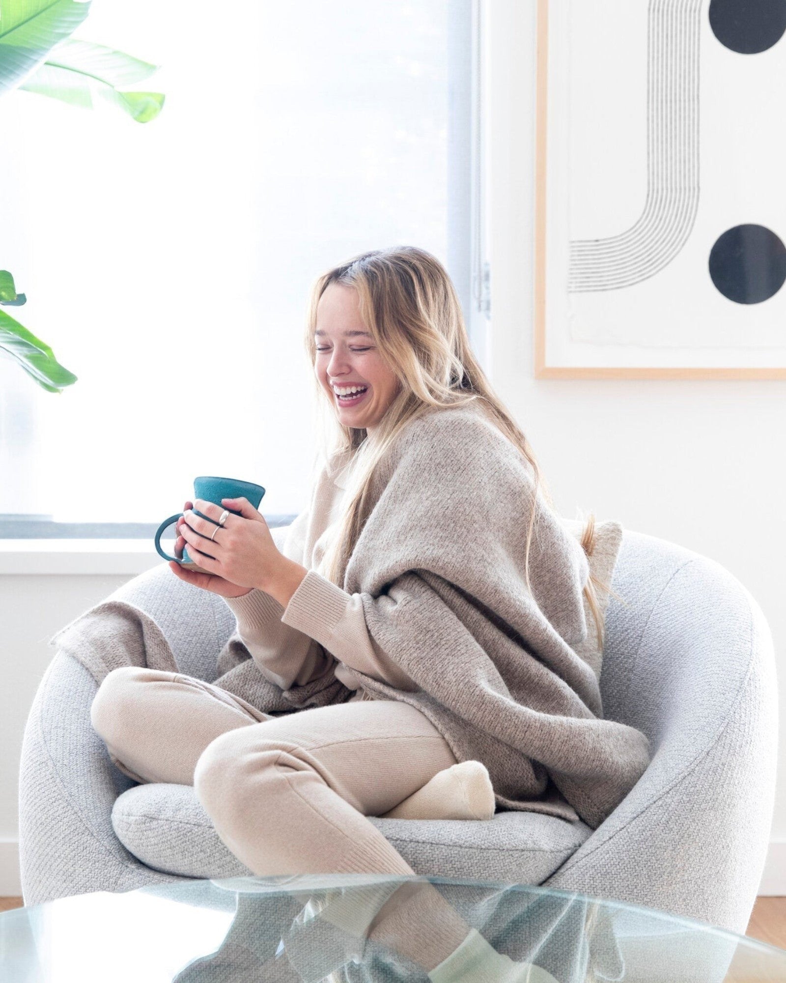 JONES + CO oatmeal alpaca wool blend throw blanket draped over a woman sitting in a chair with a mug.