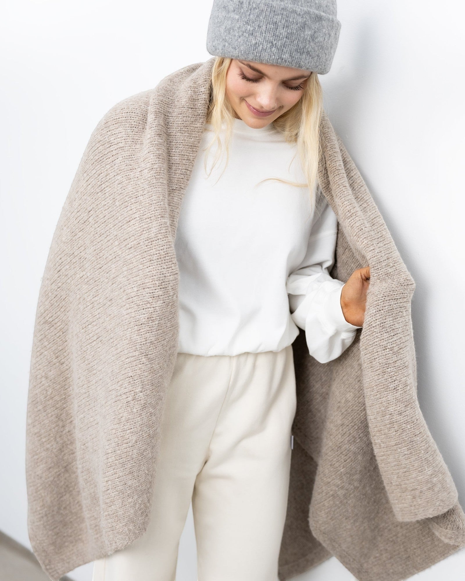 JONES + CO oatmeal alpaca wool blend throw blanket draped over a woman wearing a grey beanie and white sweater.
