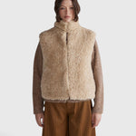 JONES + CO oatmeal high neck reversible faux fur vest with a cropped, boxy silhouette worn over a brown knit top.
