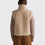 JONES + CO oatmeal high neck reversible faux fur vest worn from the back showing a boxy cropped silhouette