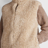 JONES + CO oatmeal high neck reversible faux fur vest with a cropped boxy fit worn over a brown knit sweater