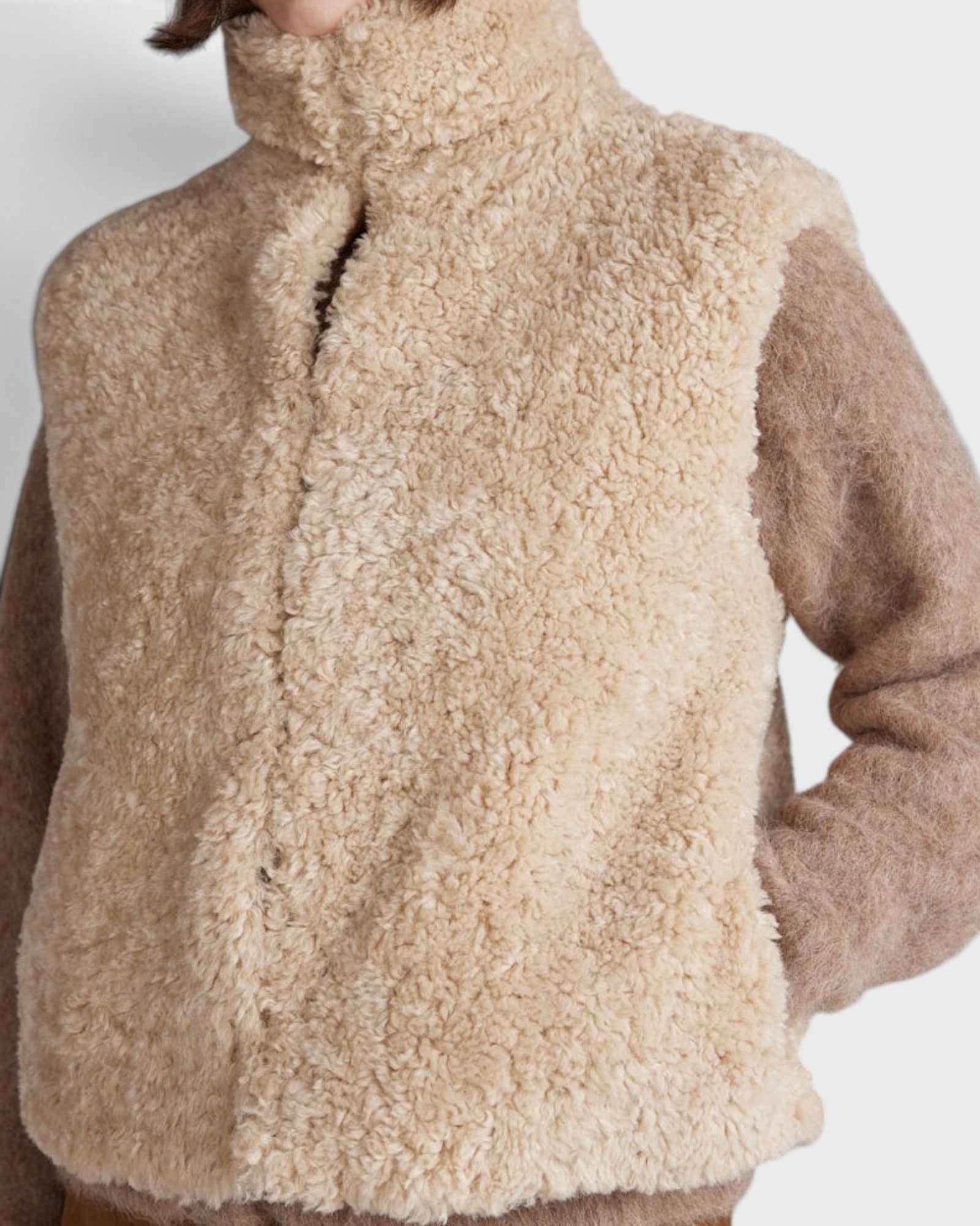 JONES + CO oatmeal high neck reversible faux fur vest with a cropped boxy fit worn over a brown knit sweater