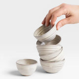 JONES + CO off-white handcrafted ceramic little bowls stacked and held by a hand against a white background