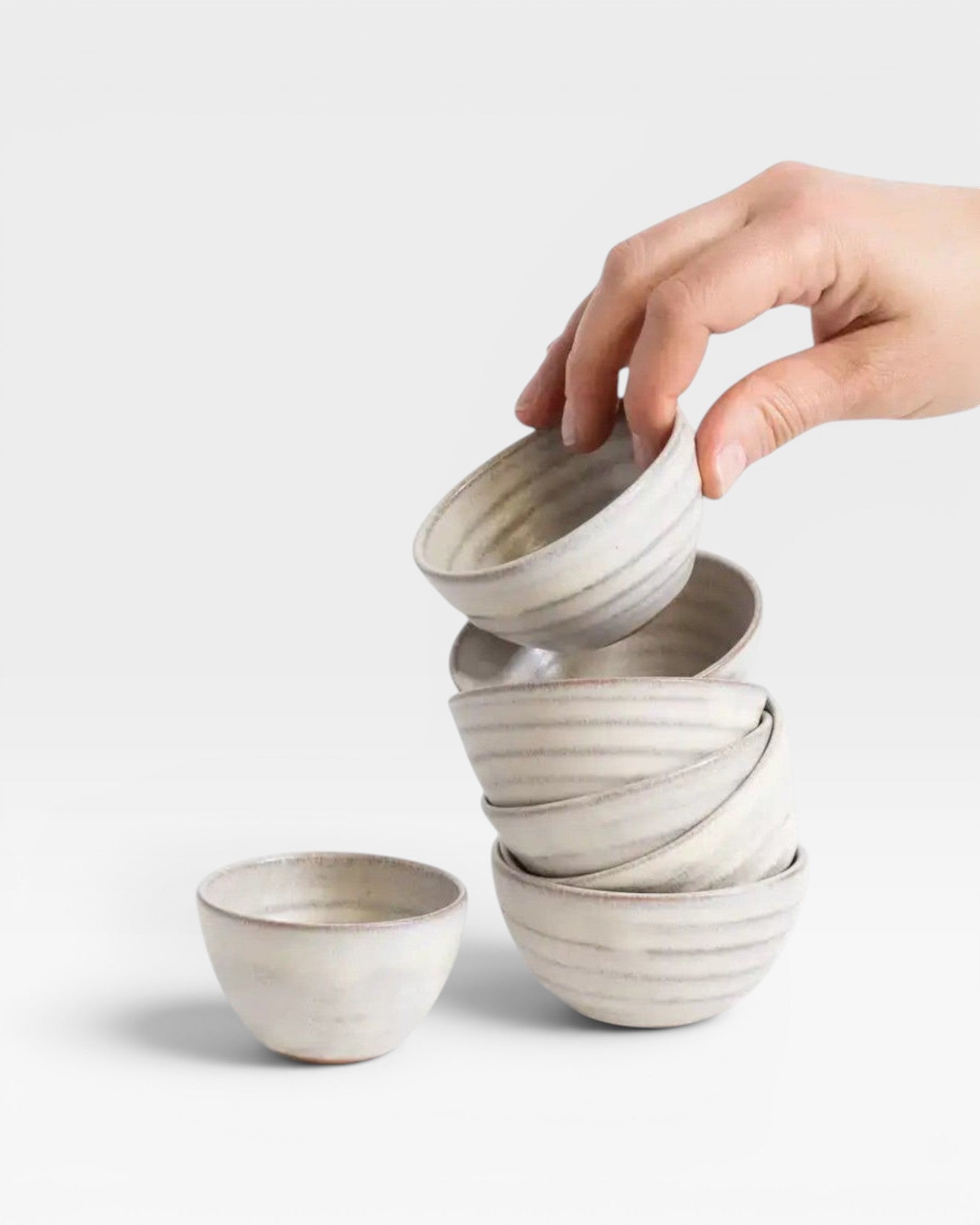 JONES + CO off-white handcrafted ceramic little bowls stacked and held by a hand against a white background