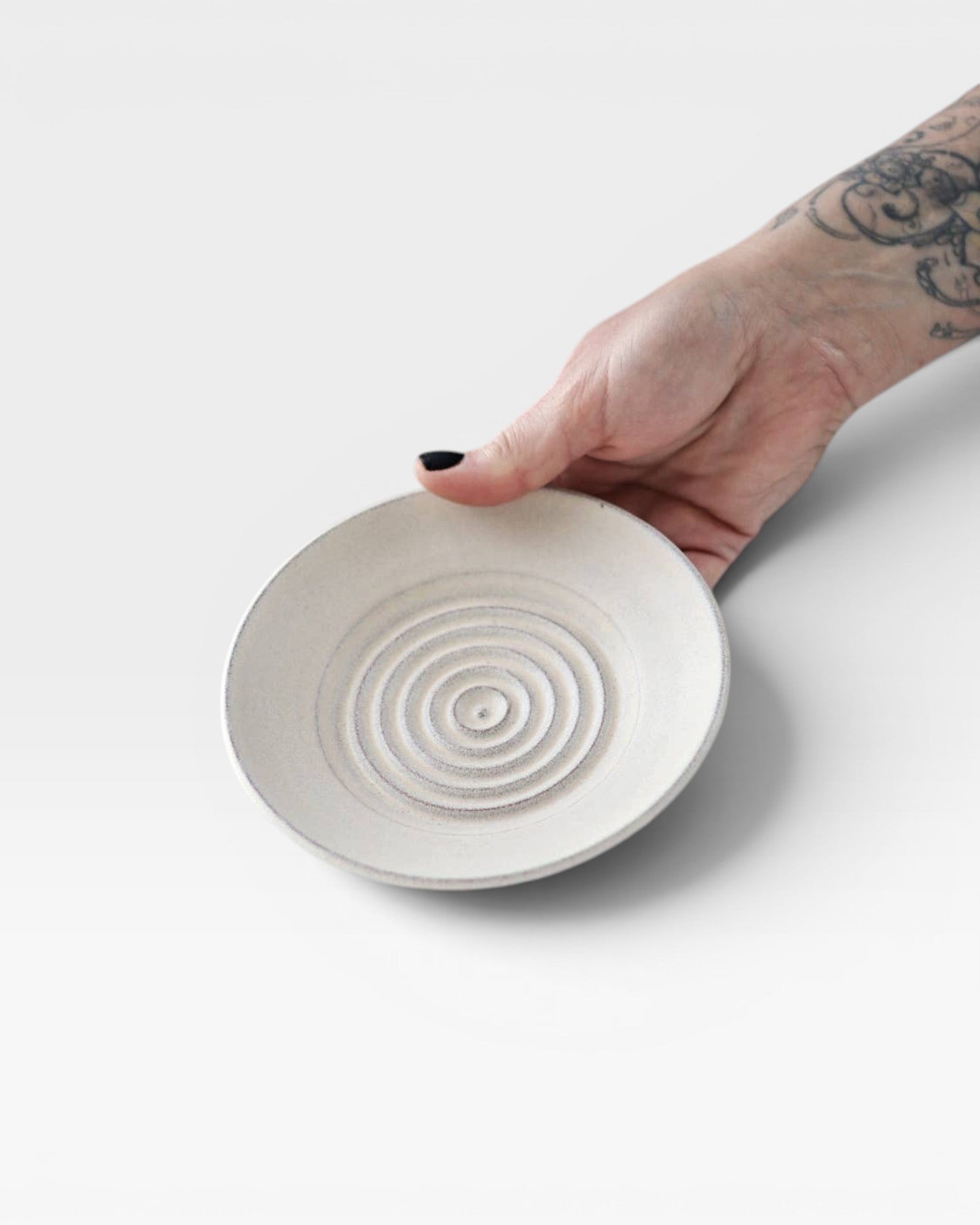 JONES + CO off-white ceramic garlic grater plate with raised circular ridges held in a hand