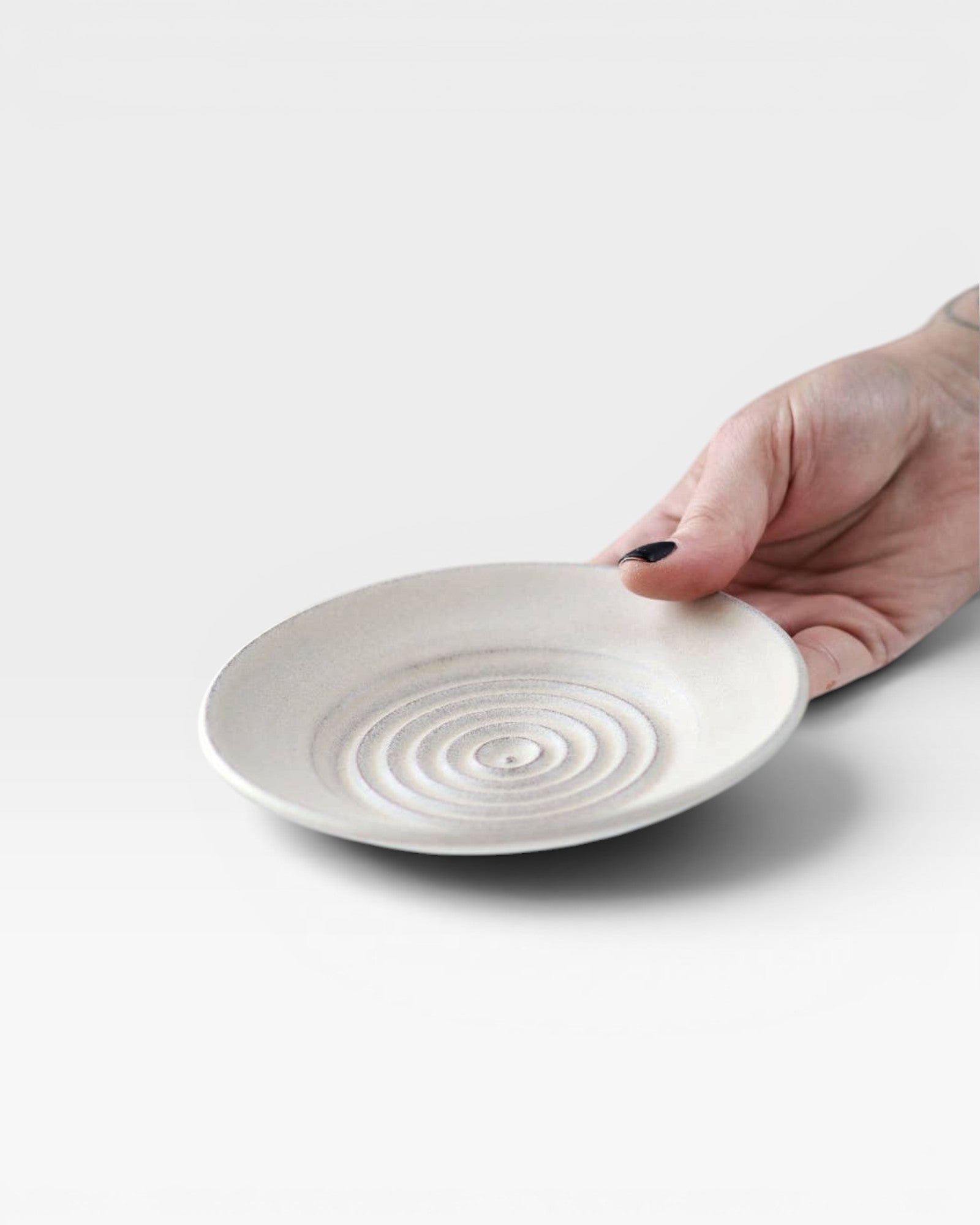 JONES + CO off-white ceramic garlic grater plate with raised spiral ridges held in a hand