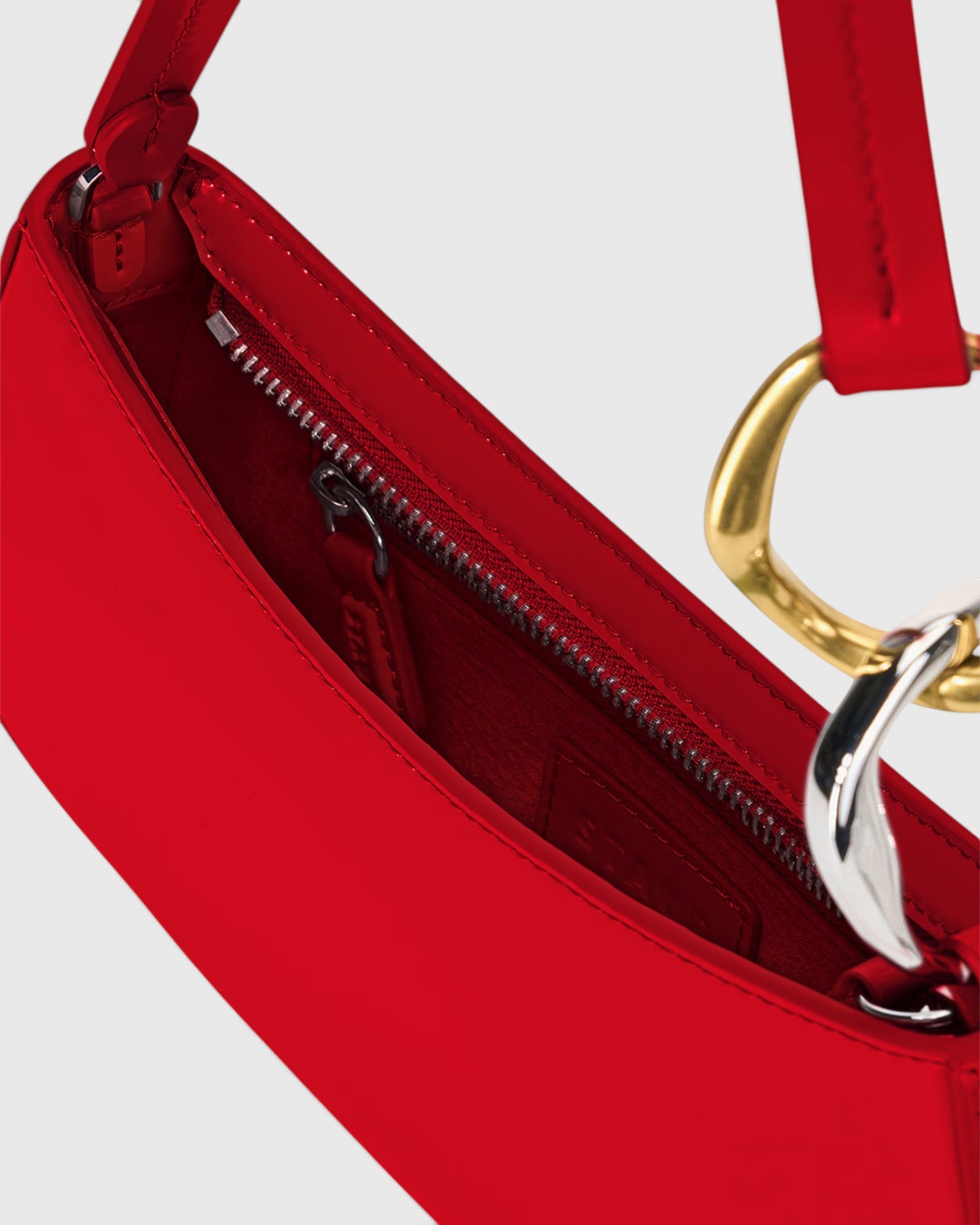 JONES + CO Ollie Bag in cherry red polished leather with a crescent shape, gold hardware, and secure zip closure.