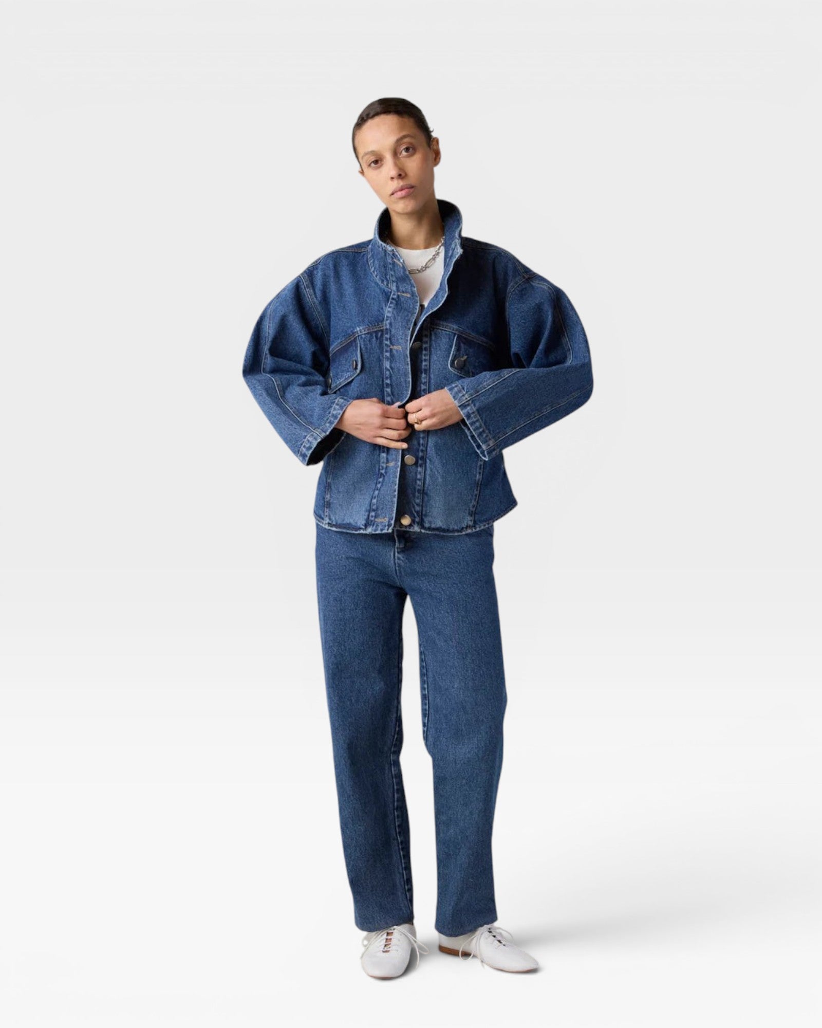 JONES + CO dark denim oversized jacket with stand collar, asymmetric snap closure, and flap pockets. Model wears it with matching jeans.