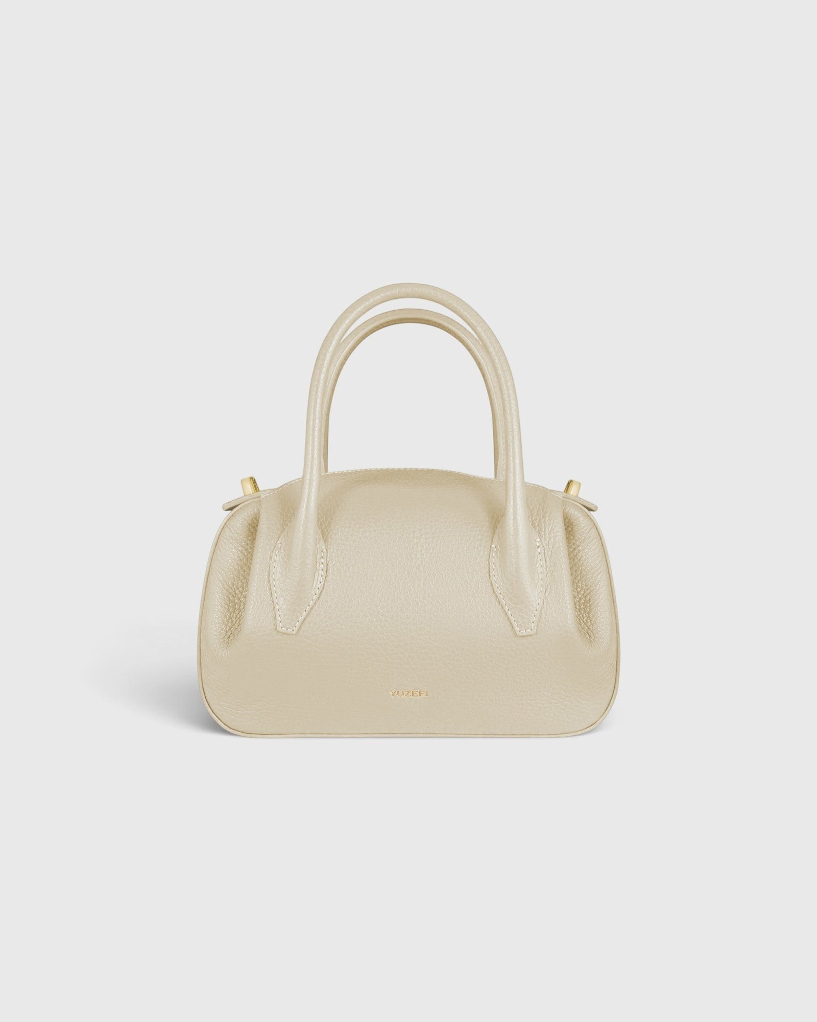 JONES + CO Oyster Mini Duffle in angora pebble grained leather with gold-tone hardware and structured top handles.