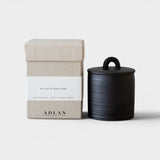 JONES + CO Plague Doctor petite candle in a black stoneware vessel next to its beige textured gift box