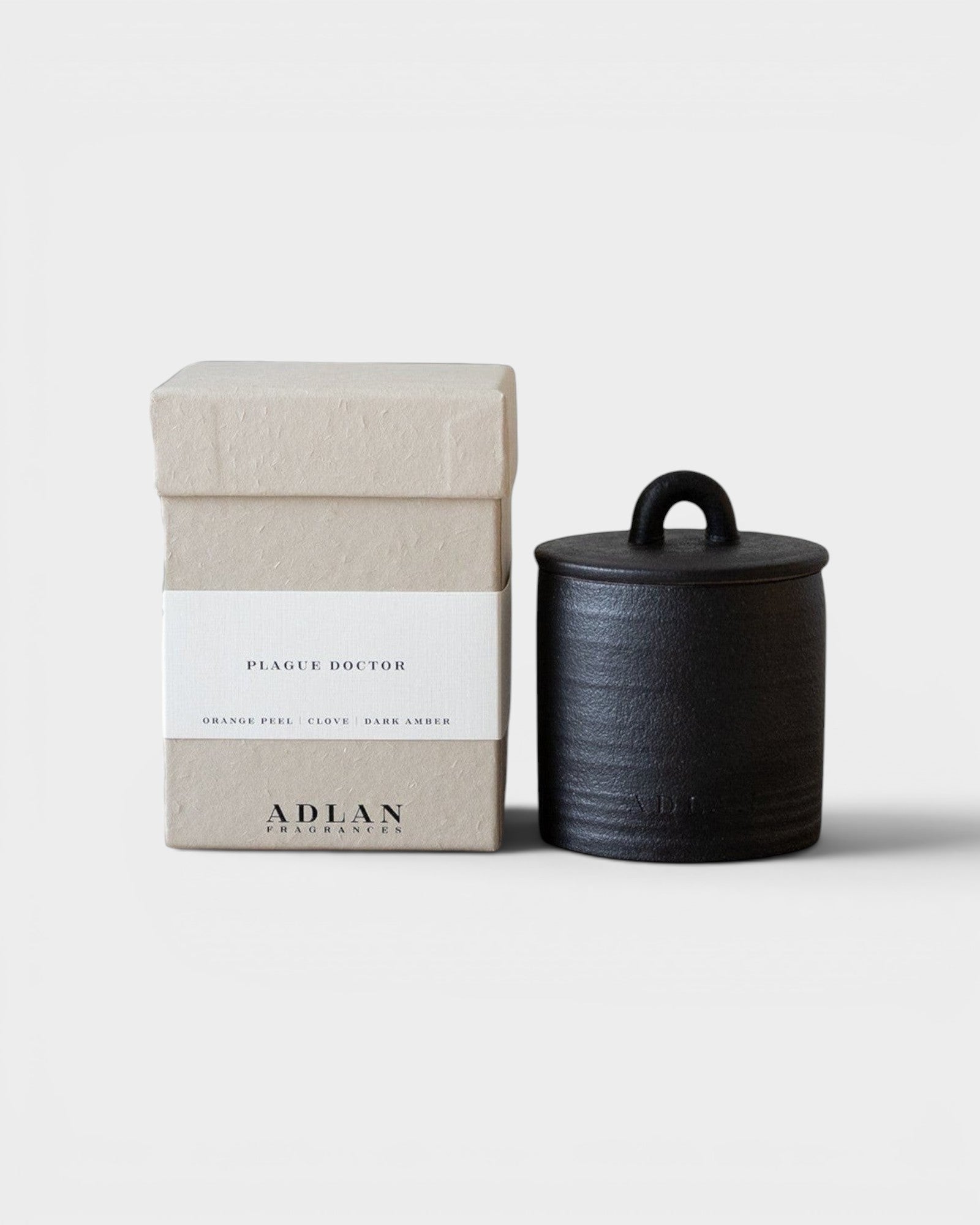 JONES + CO Plague Doctor petite candle in a black stoneware vessel next to its beige textured gift box