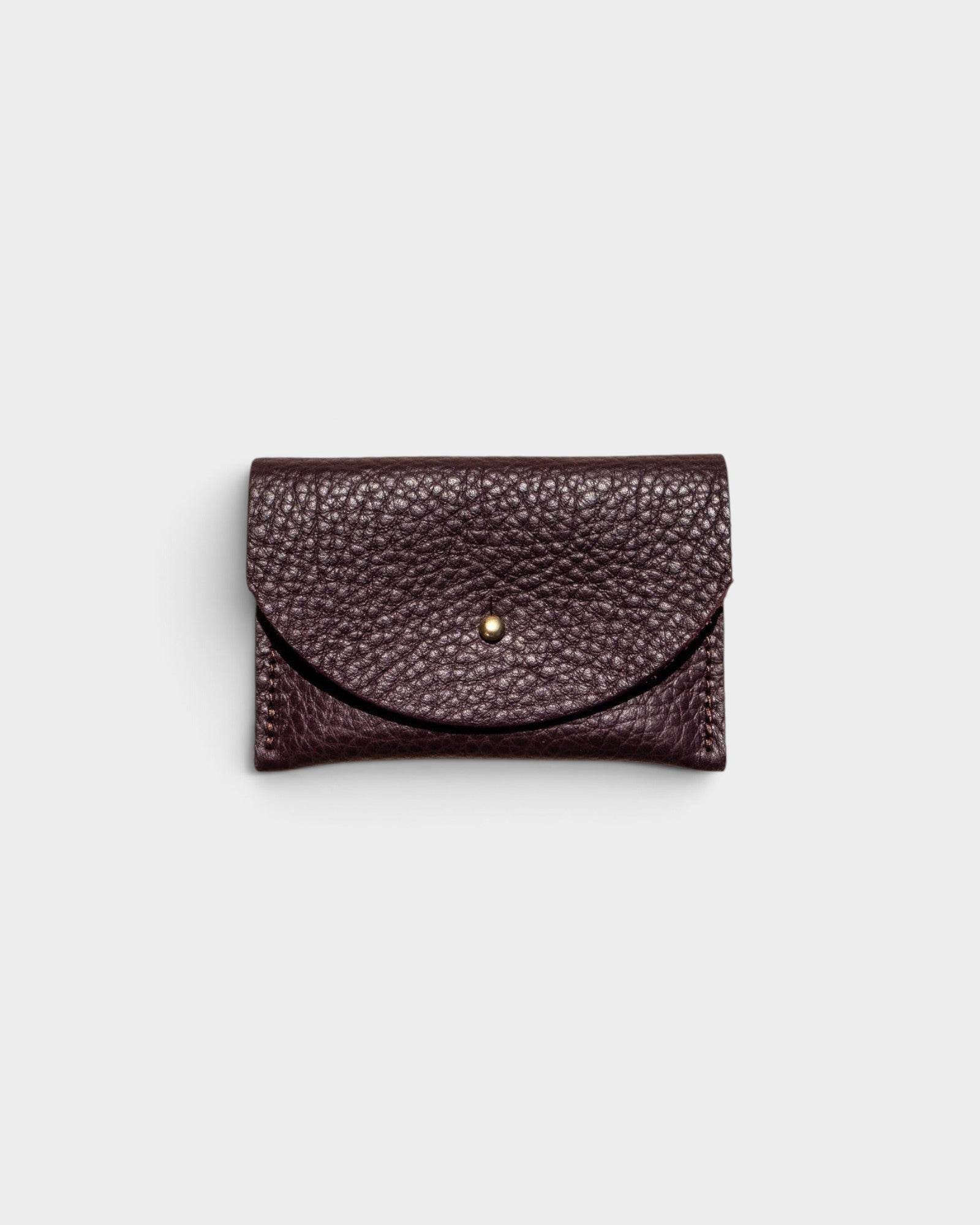 JONES + CO plum leather cardholder with a solid brass fastener and textured finish on a light grey background