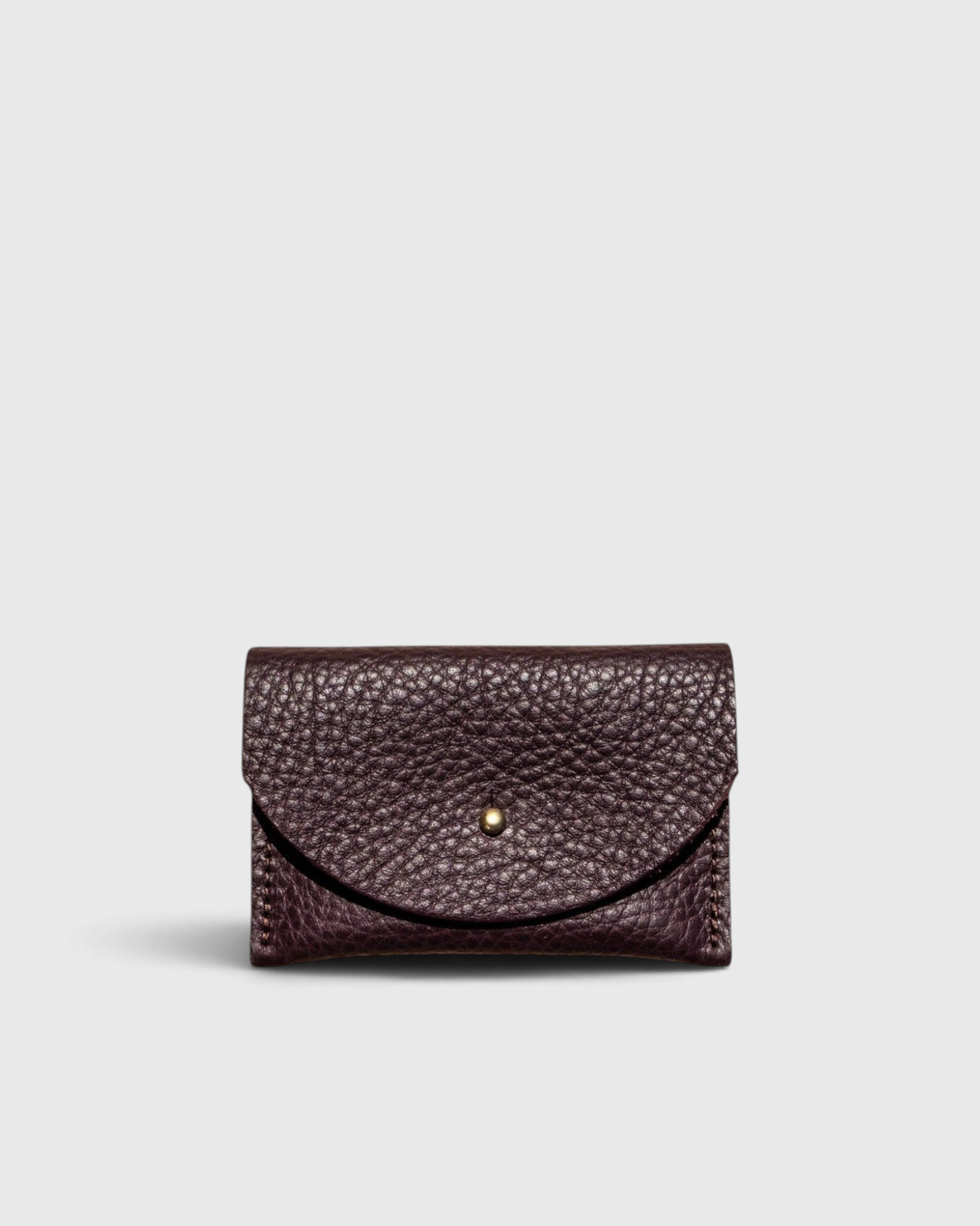 JONES + CO plum leather cardholder with a solid brass fastener and textured finish on a light grey background