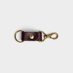 JONES + CO plum leather keychain with solid brass keyring and clip hardware on a light grey background.