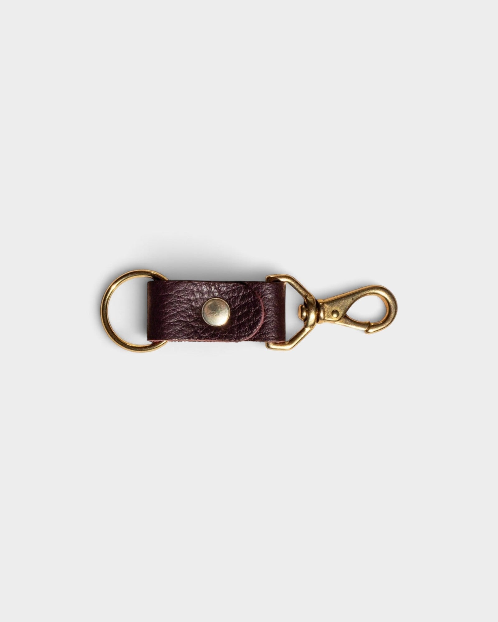 JONES + CO plum leather keychain with solid brass keyring and clip hardware on a light grey background.