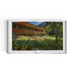 JONES + CO Private Aspen book open to a photograph of a modern wooden house set in a lush mountain meadow.