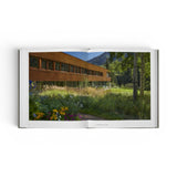 JONES + CO Private Aspen book open to a photograph of a modern wooden house set in a lush mountain meadow.