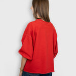 Model wearing a red JONES + CO Fond sweatshirt with drop shoulders, cropped sleeves, and a raw edge hemline.